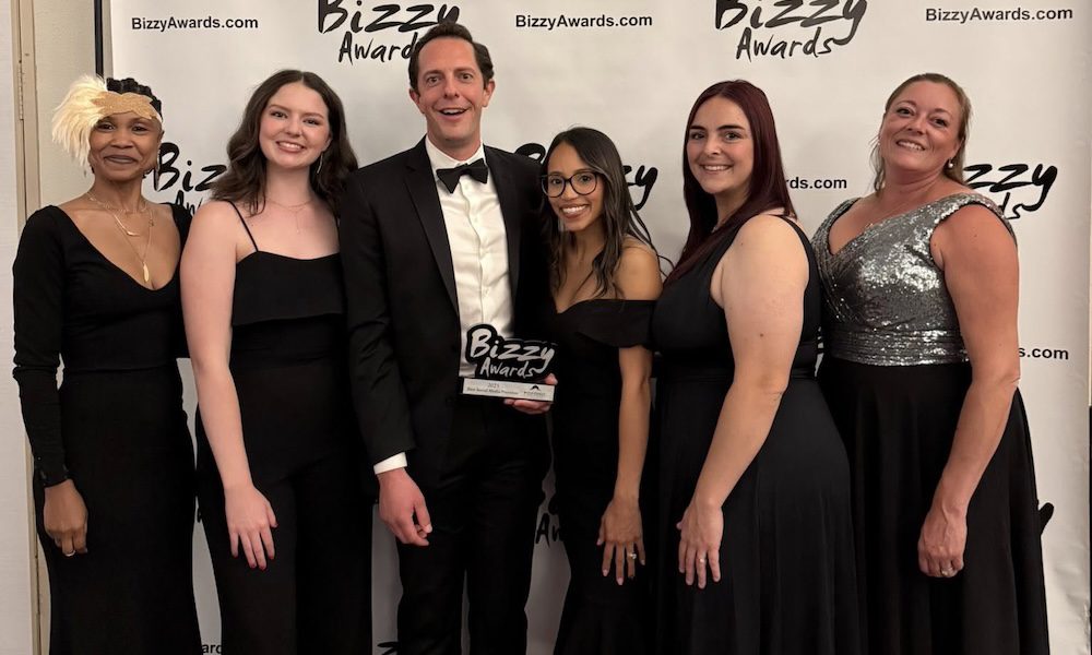 The YMI team posing together on the red carpet at the 2025 Bizzy Awards in front of the Bizzy Awards backdrop. They’re dressed in formal black and silver attire, smiling and holding the Best Social Media Presence award.