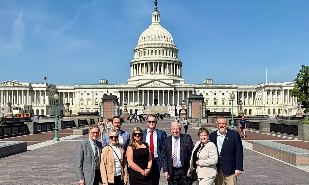 Jimi Honochick standing with a group in front of the U.S. Capitol building on a clear day, posing on the walkway with the Capitol dome centered behind them.