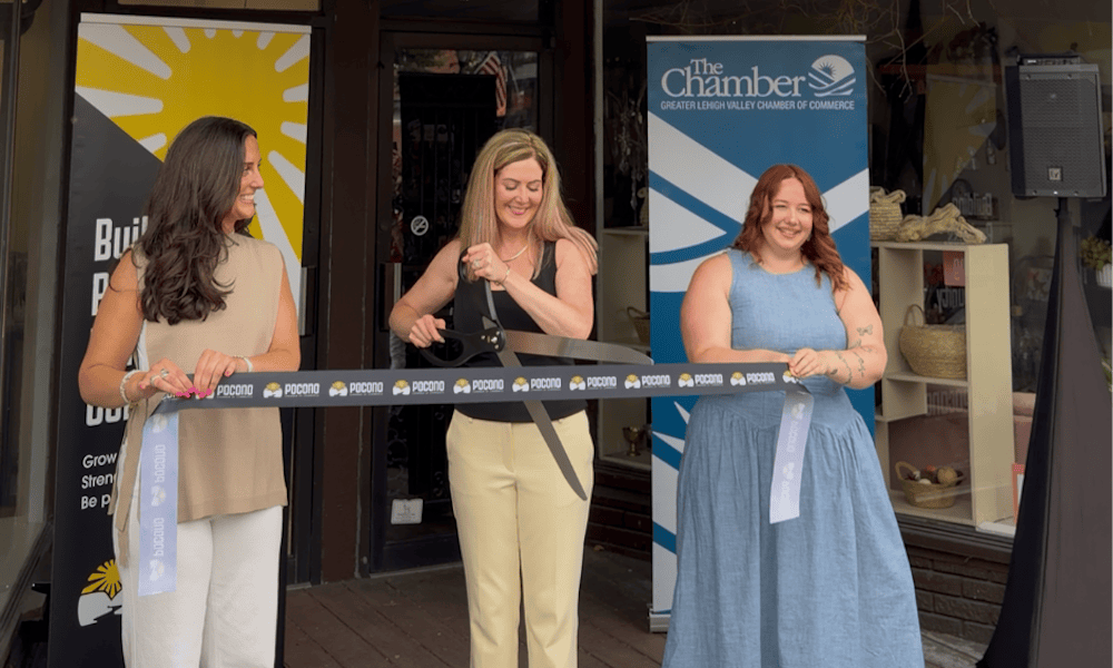 Pocono Chamber ribbon-cutting ceremony outside a local business as three women hold ceremonial ribbon and oversized scissors, celebrating the grand opening with Chamber banners in the background.